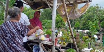 Sukini relawan pembersih TPU Dusun Krajan, Desa Genteng Kulon, Kecamatan Genteng yang juga penjual bunga tabur musiman saat melayani pembeli di lapaknya, Rabu (22/3/2023).(blok-a.com/Kuryanto)