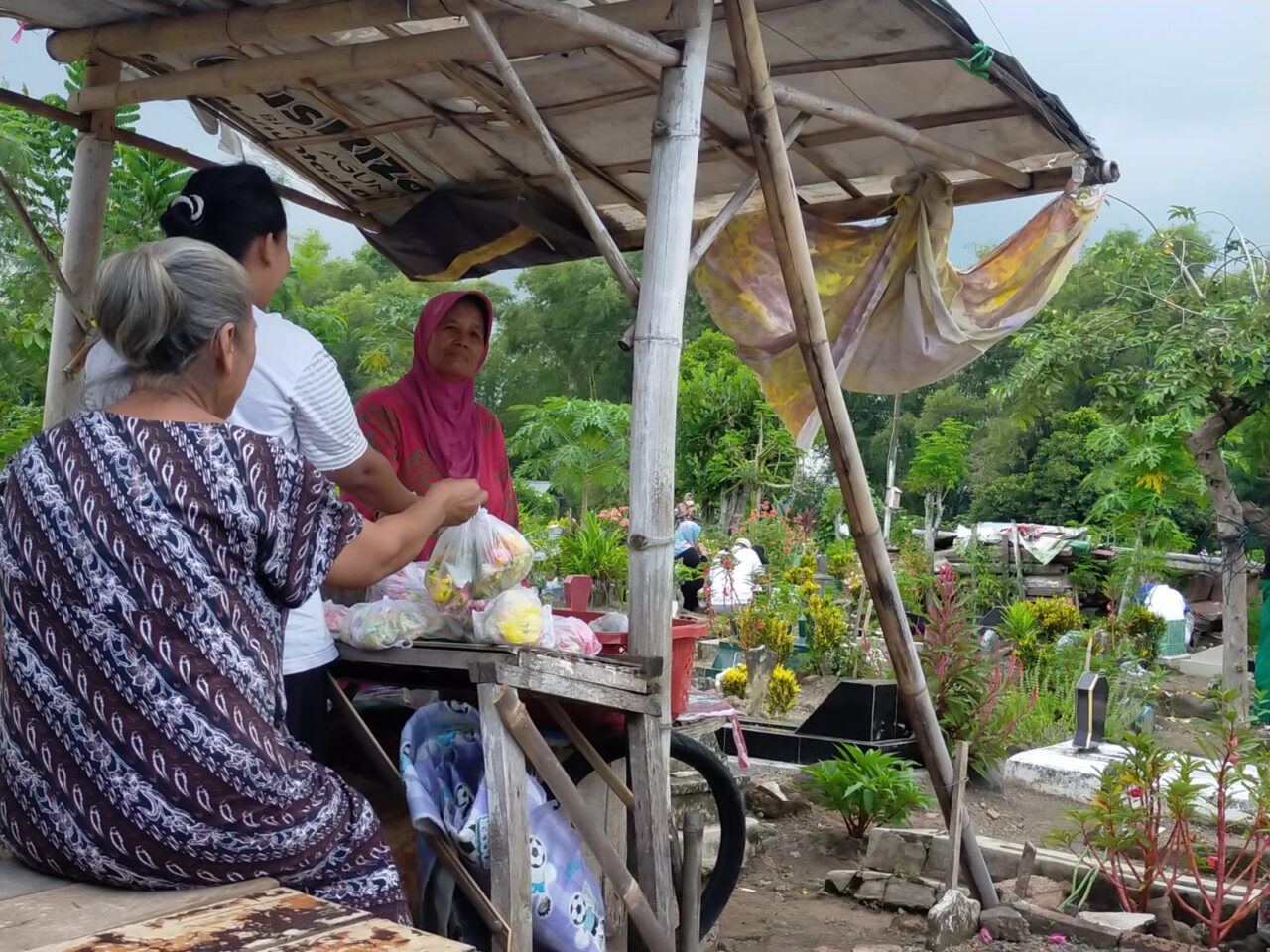 Sukini relawan pembersih TPU Dusun Krajan, Desa Genteng Kulon, Kecamatan Genteng yang juga penjual bunga tabur musiman saat melayani pembeli di lapaknya, Rabu (22/3/2023).(blok-a.com/Kuryanto)