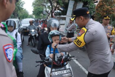 Kapolres Blitar Kota, AKBP Titus Yudho Uly memasangkan helm kepada anak-anak yang hendak ke sekolah. (blok-a.com/Fajar)