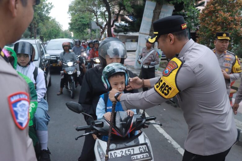 Kapolres Blitar Kota, AKBP Titus Yudho Uly memasangkan helm kepada anak-anak yang hendak ke sekolah. (blok-a.com/Fajar)