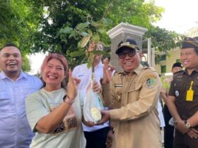 Caption : Wakil Bupati Banyuwangi, Mujiono saat menyerahkan bibit pohon kepada salah satu warga yang melintas di depan Kantor Perum Perhutani Banyuwangi, Senin (5/1/2026).