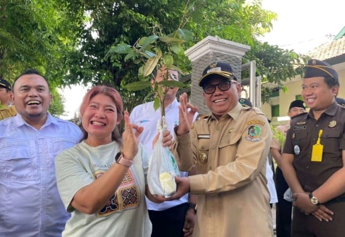 Caption : Wakil Bupati Banyuwangi, Mujiono saat menyerahkan bibit pohon kepada salah satu warga yang melintas di depan Kantor Perum Perhutani Banyuwangi, Senin (5/1/2026).