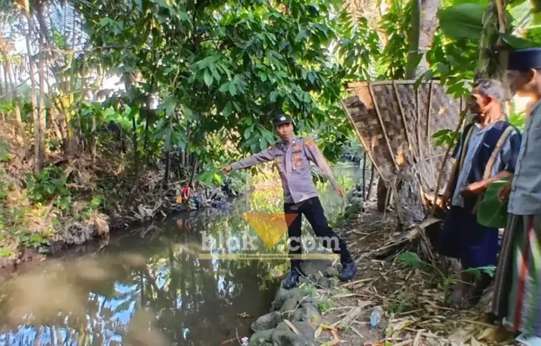 Kanit Intelkam Polsek Singojuruh, Aiptu Firdaus saat menunjukkan lokasi ditemukan Muawanah, lansia yang meninggal dunia di sungai belakang rumahnya, Senin (06/07/2026)(foto: Blok-a.com/Kuryanto)
